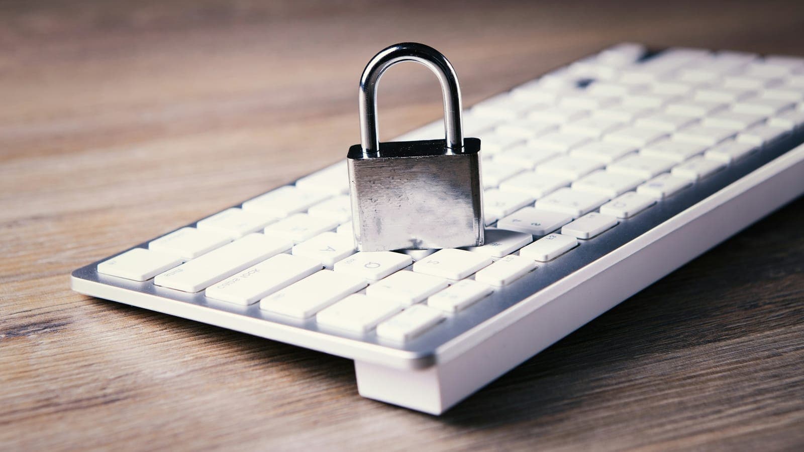 Closed padlock on a white keyboard on a wooden desk