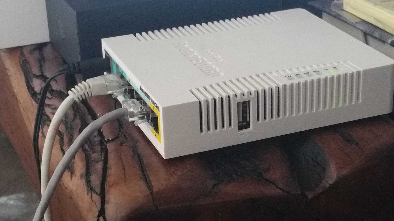 White MikroTik router on a wooden table, with several network cables plugged into its ports
