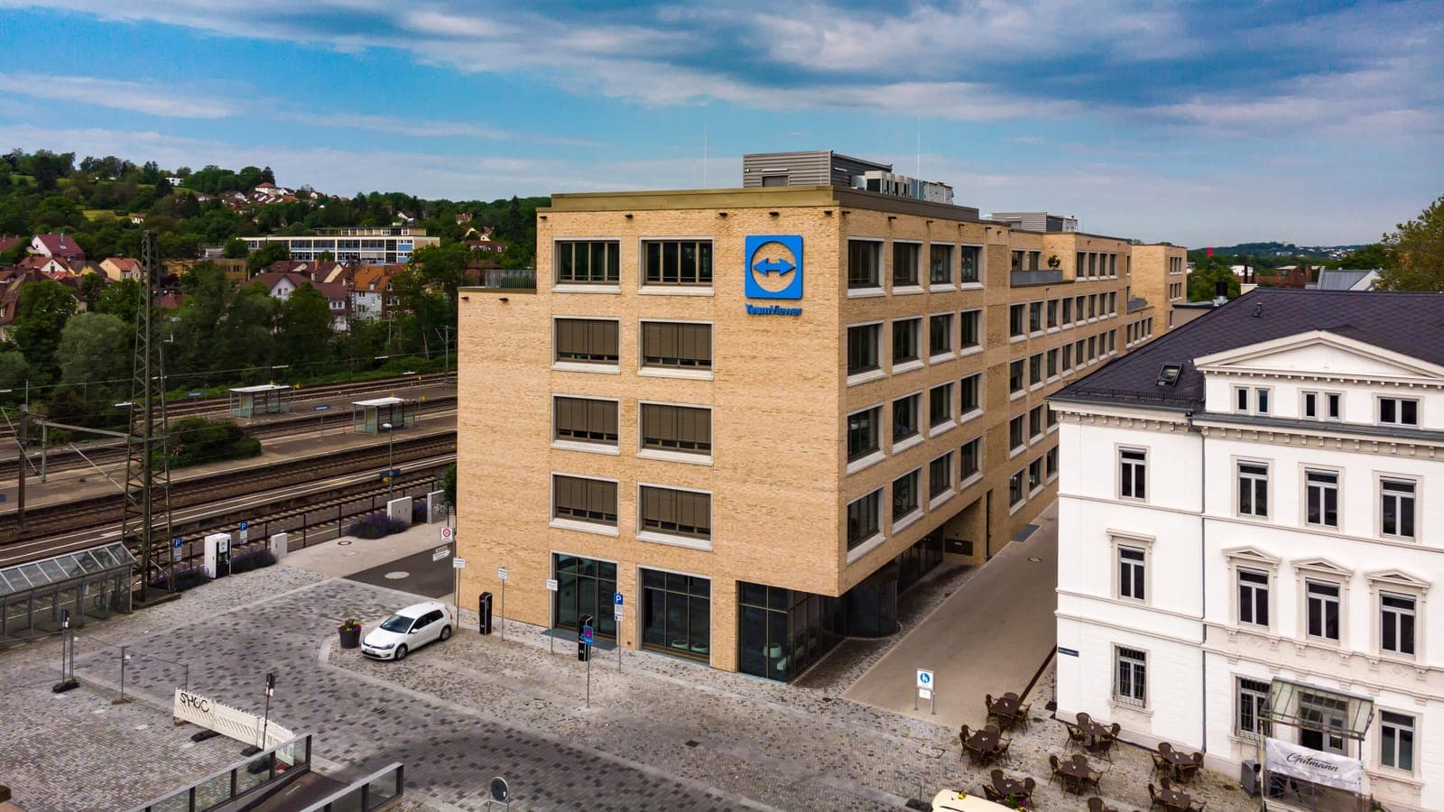 Aerial view of TeamViewer's office building in Göppingen (Germany), in light brick with the logo on the façade, next to the railway tracks